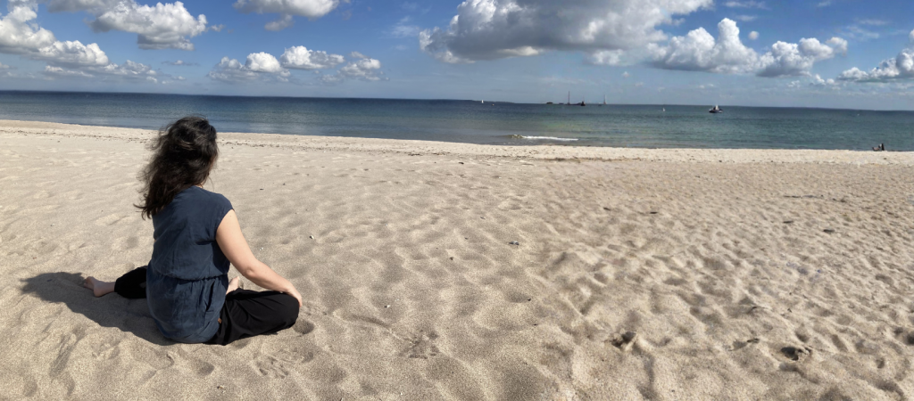 Frau sitzt ruhig am Strand und blickt aufs Meer – Symbol für Pause und raus aus dem Funktionieren